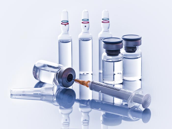 On a sterile reflective surface are arranged a group of glass ampoules, metal-topped vials, and a surgical needle.